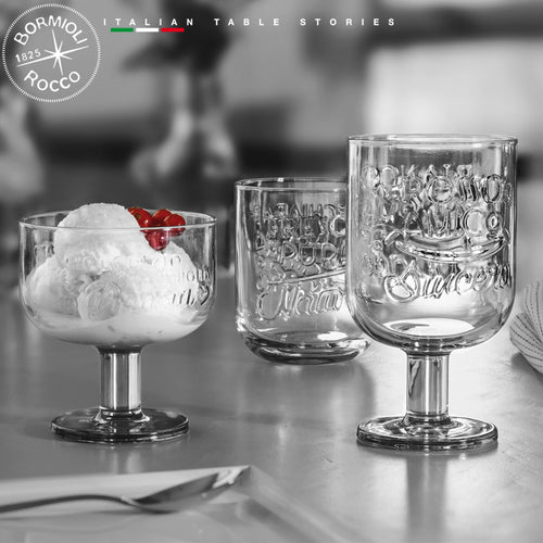 Set di bicchieri e coppa in vetro trasparente con decorazioni in rilievo, uno con gelato e ciliegie su tavolo.