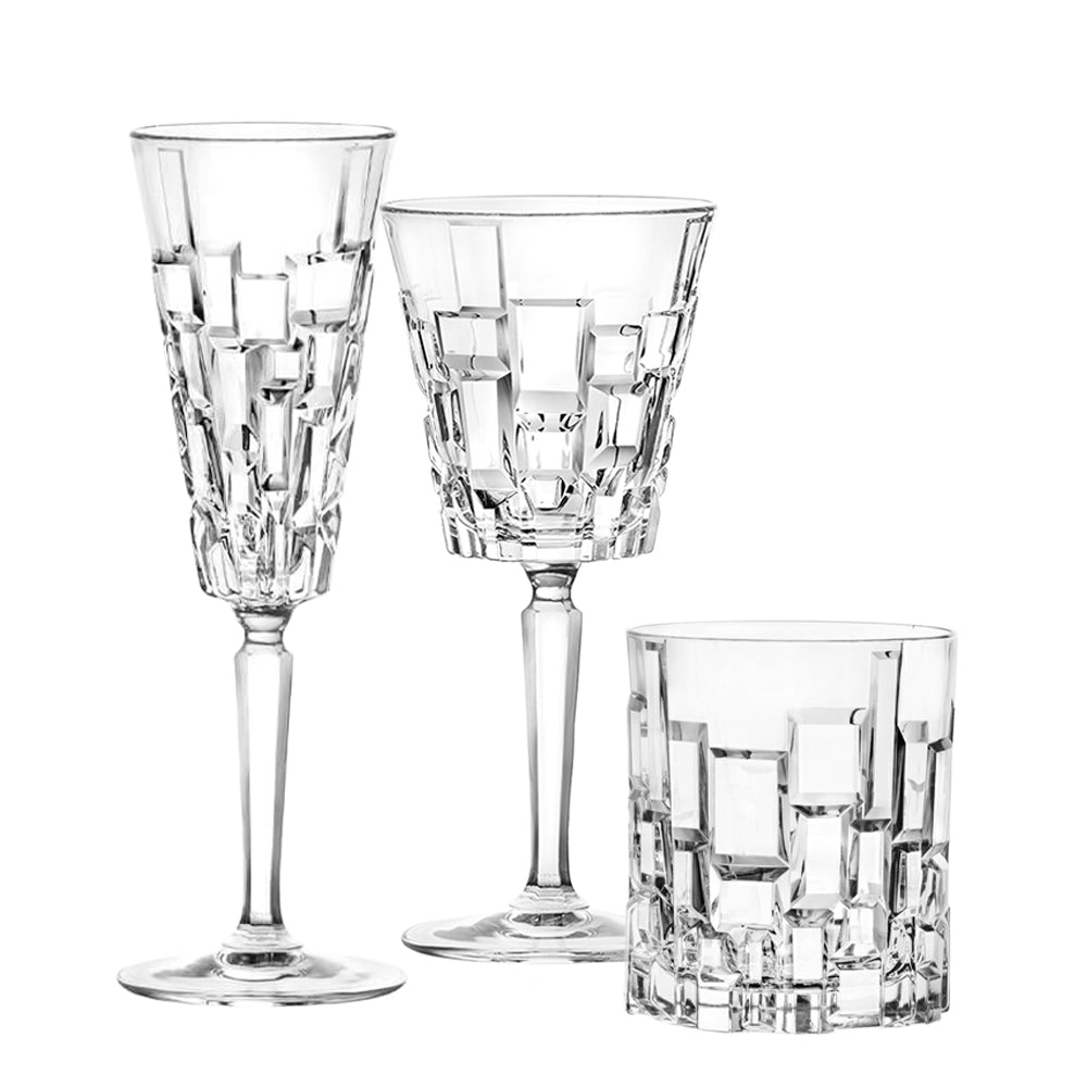 Tre bicchieri di cristallo trasparente con decori geometrici a rilievo, un calice da vino, un flute e un tumbler, sfondo bianco.