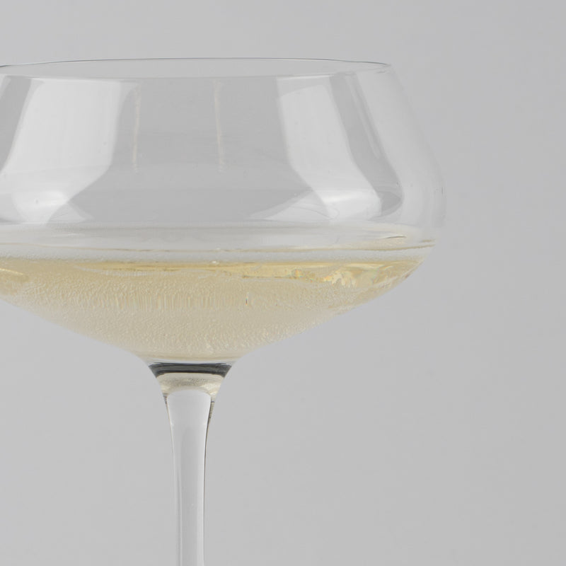 calice di vetro trasparente con liquido frizzante di colore chiaro su sfondo grigio uniforme