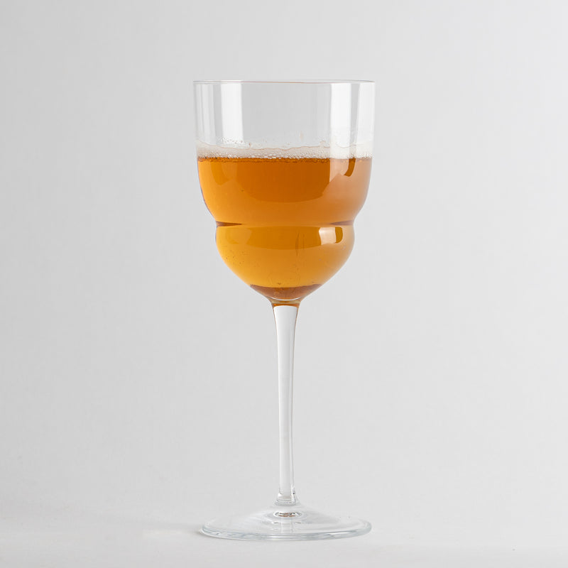 calice di vetro trasparente con gambo lungo contenente bevanda arancione schiumosa su sfondo bianco