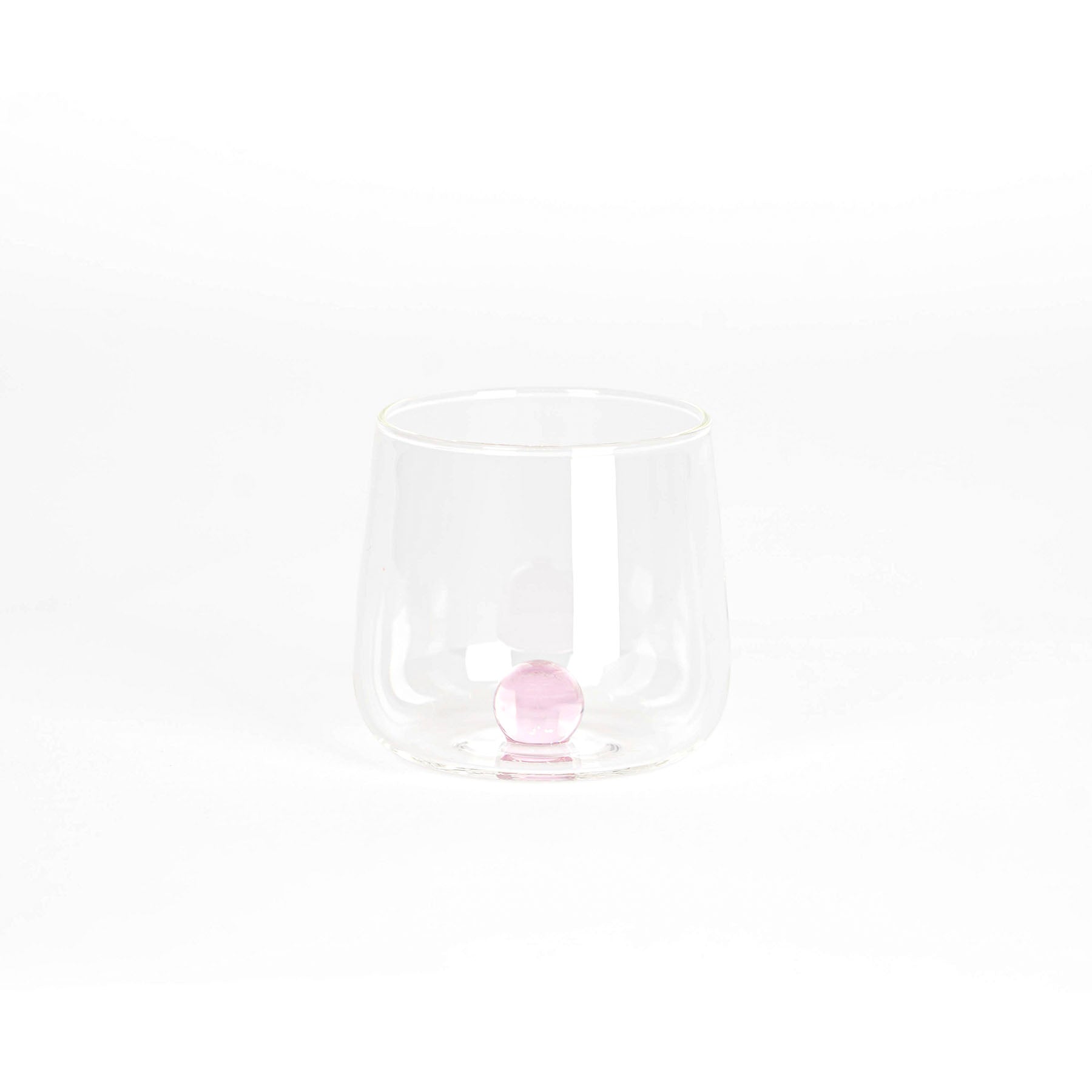 bicchiere trasparente in vetro con base arrotondata contenente una sfera rosa al centro, su sfondo bianco uniforme