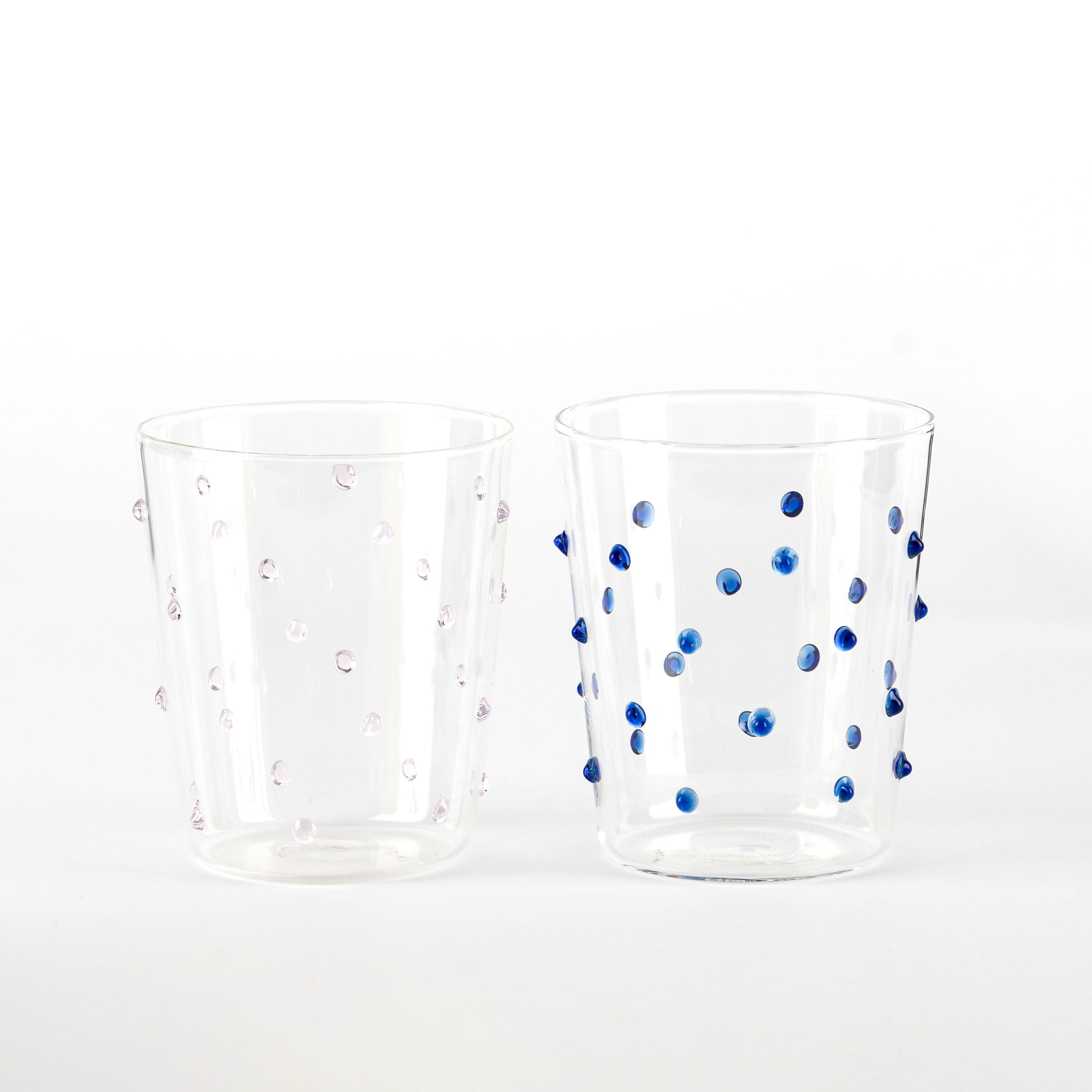 Due bicchieri trasparenti in vetro con puntini sporgenti, uno con punti rosa e l'altro con punti blu, su sfondo bianco.