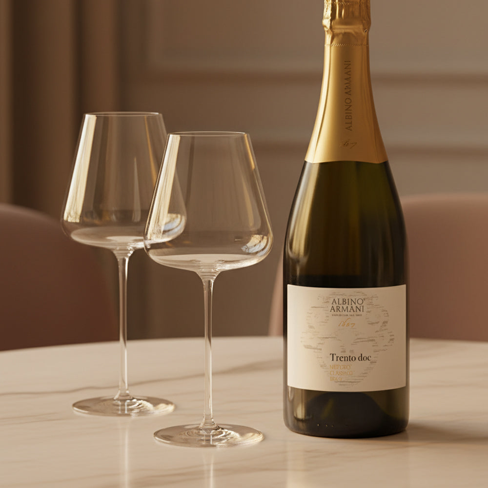 Bottiglia di vino Albino Armani Trento DOC con tappo dorato e due calici di vetro trasparente su tavolo in marmo bianco.