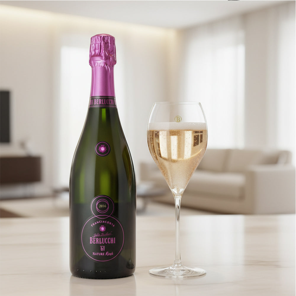 Bottiglia di spumante Berlucchi 61 con tappo rosa, accanto a un calice di vino con bollicine, su un tavolo in un ambiente luminoso.