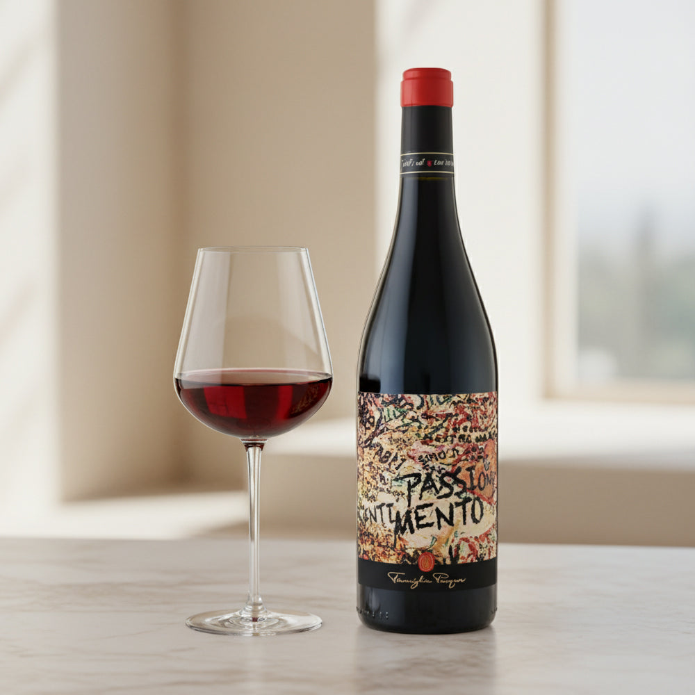 Bottiglia di vino rosso con etichetta colorata, accanto a un bicchiere pieno di vino, su un tavolo chiaro in un ambiente luminoso.