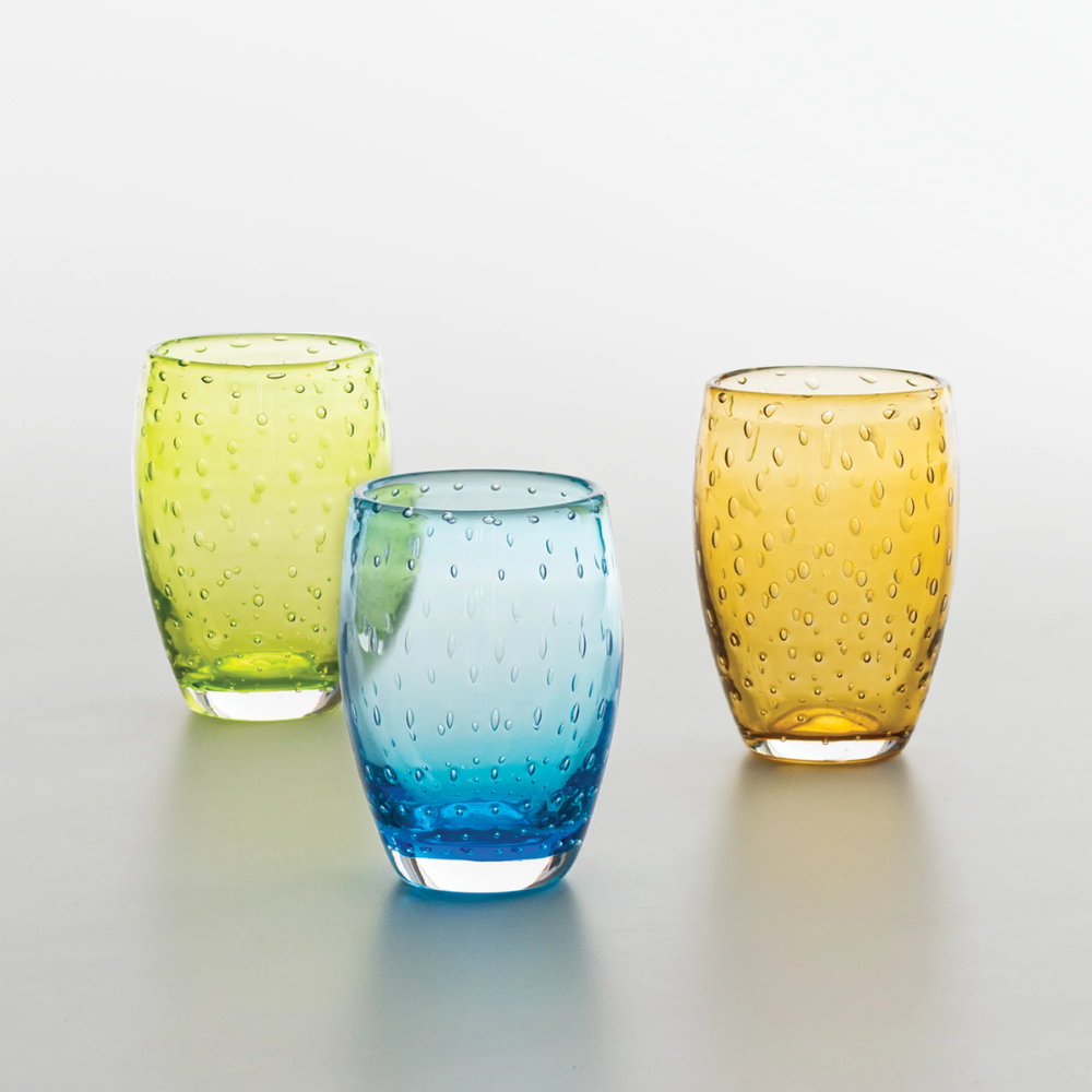 tre bicchieri di vetro colorato verde, azzurro e ambra con decorazione a rilievo a puntini su sfondo neutro chiaro