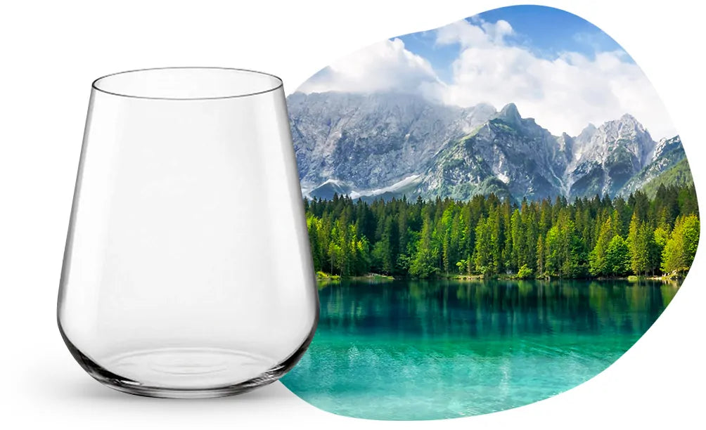 bicchiere trasparente in vetro con forma conica rovesciata su sfondo bianco e paesaggio montano con lago e