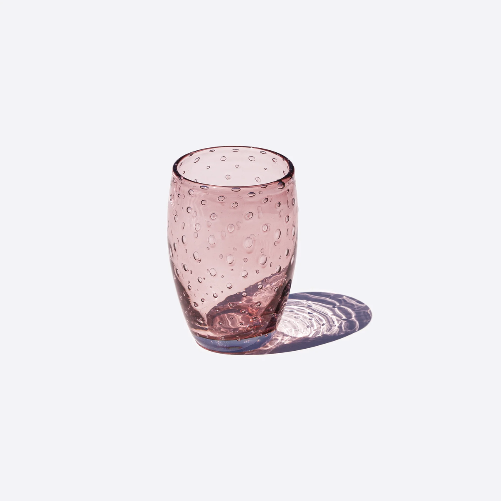 Bicchiere rosa trasparente in vetro con bolle interne, su sfondo bianco con ombra riflessa.