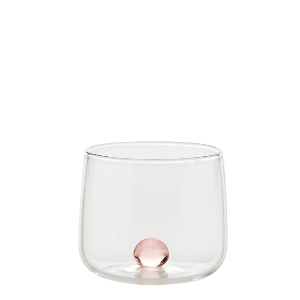 bicchiere trasparente in vetro con pallina rosa incastonata sul fondo, sfondo bianco neutro
