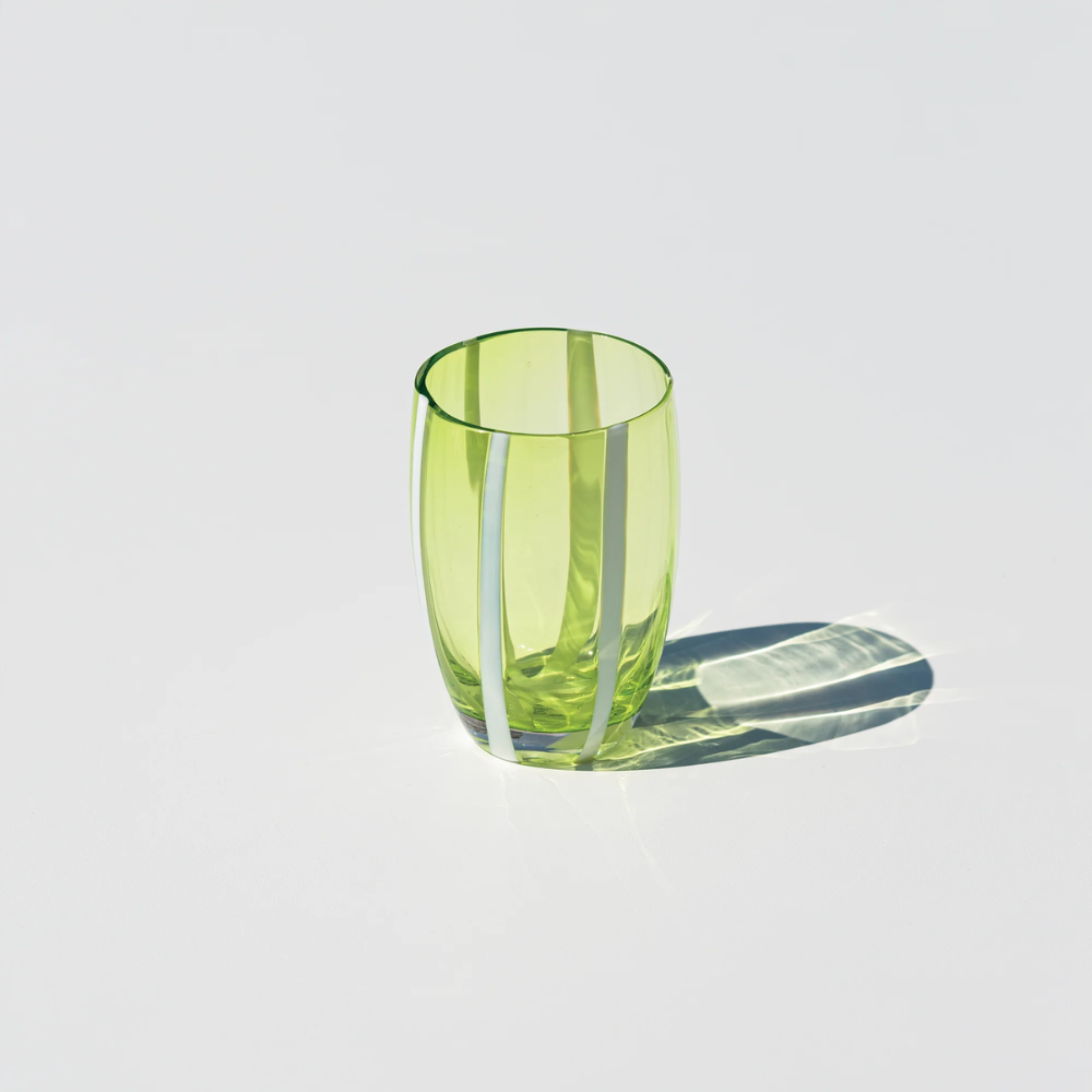 Bicchiere di vetro verde trasparente con strisce bianche verticali su sfondo bianco e ombra proiettata.