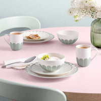 Set di stoviglie in ceramica bianca con decorazioni verdi, secondo piatto, ciotola con yogurt e kiwi, tazza con caffè, su tavolo rosa.