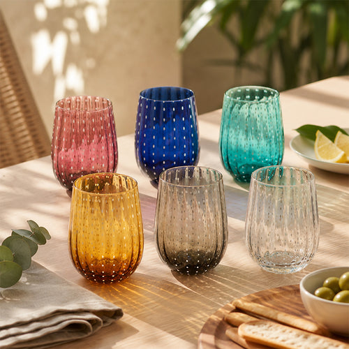6 Bicchieri colorati, Ametista, Blu, Celeste, Giallo, Grigio e Trasparente su una tavola.