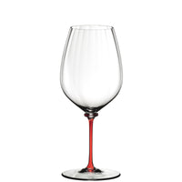 Calice da vino in vetro trasparente con gambo sottile di colore rosso isolato su sfondo bianco.