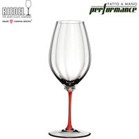 Bicchiere da vino trasparente con gambo rosso, forma slanciata e design artigianale Riedel Performance su sfondo bianco.