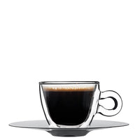 Café negro con espuma en cristal transparente sobre platillo redondo gris sobre fondo blanco