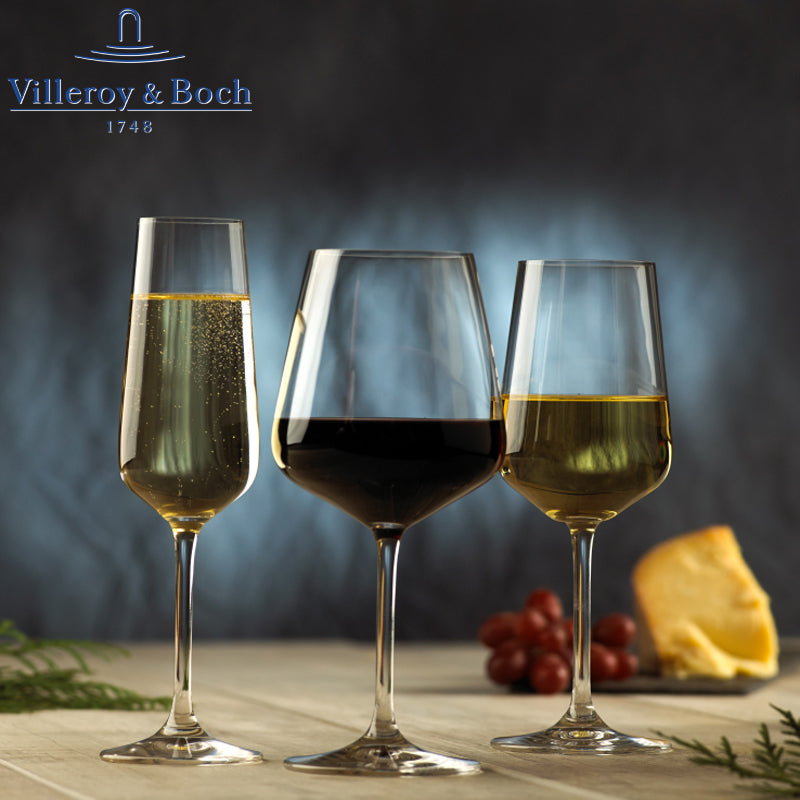 Tre bicchieri di vino (spumante, rosso e bianco) su un tavolo di legno, accompagnati da formaggio e grappolo d'uva. Sfondo sfocato.
