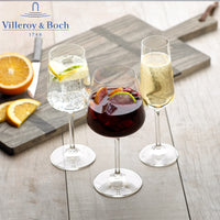 Tre calici di vetro con diverse bevande: un cocktail rosso, un drink con lime e uno spumante, accanto a fette d'arancia su un tagliere di legno.