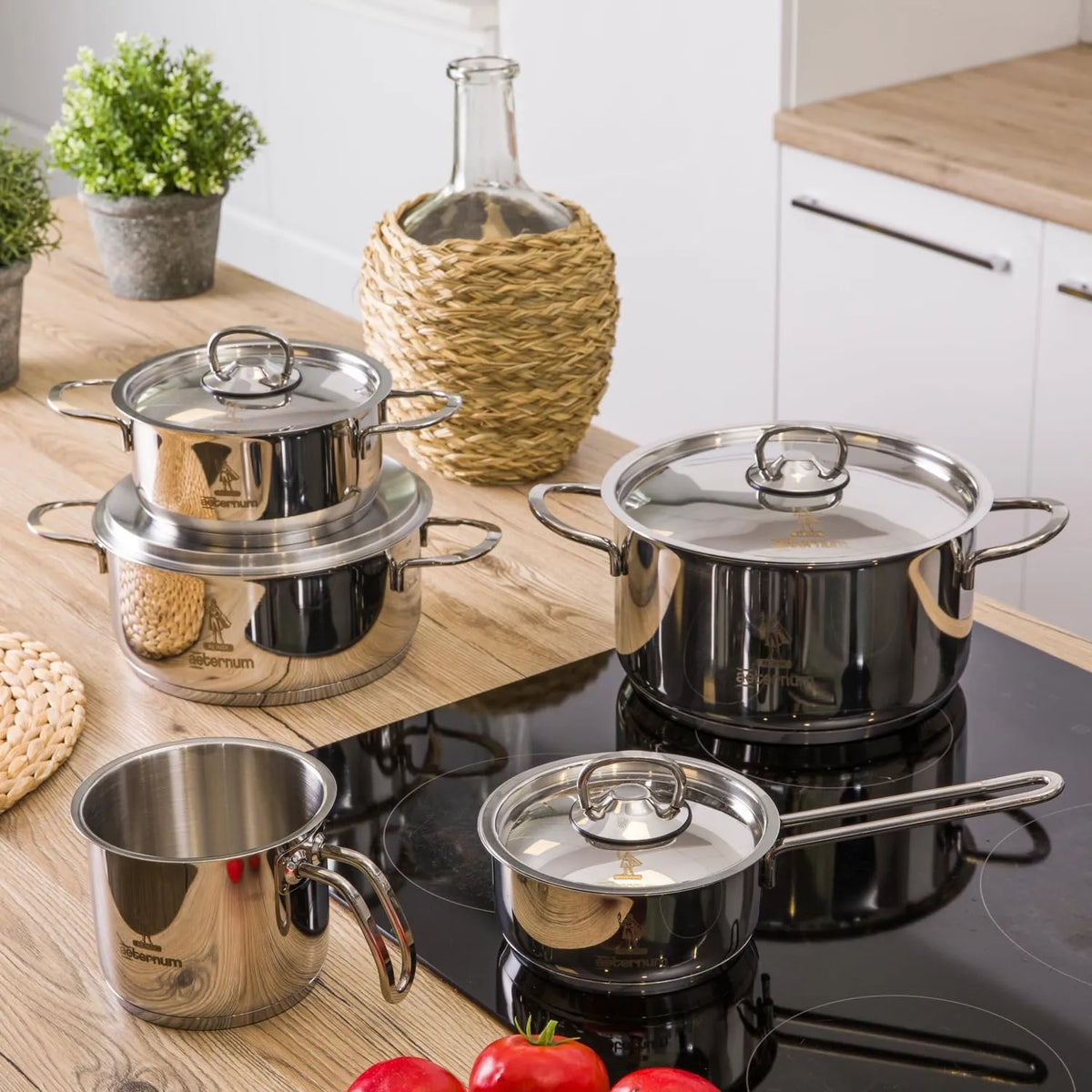 Set di pentole e casseruole in acciaio inox lucido con coperchi trasparenti su piano cottura e tavolo in