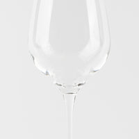 Calice da vino trasparente in vetro con gambo lungo su sfondo bianco uniforme.