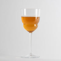 calice di vetro trasparente con gambo lungo contenente bevanda arancione schiumosa su sfondo bianco