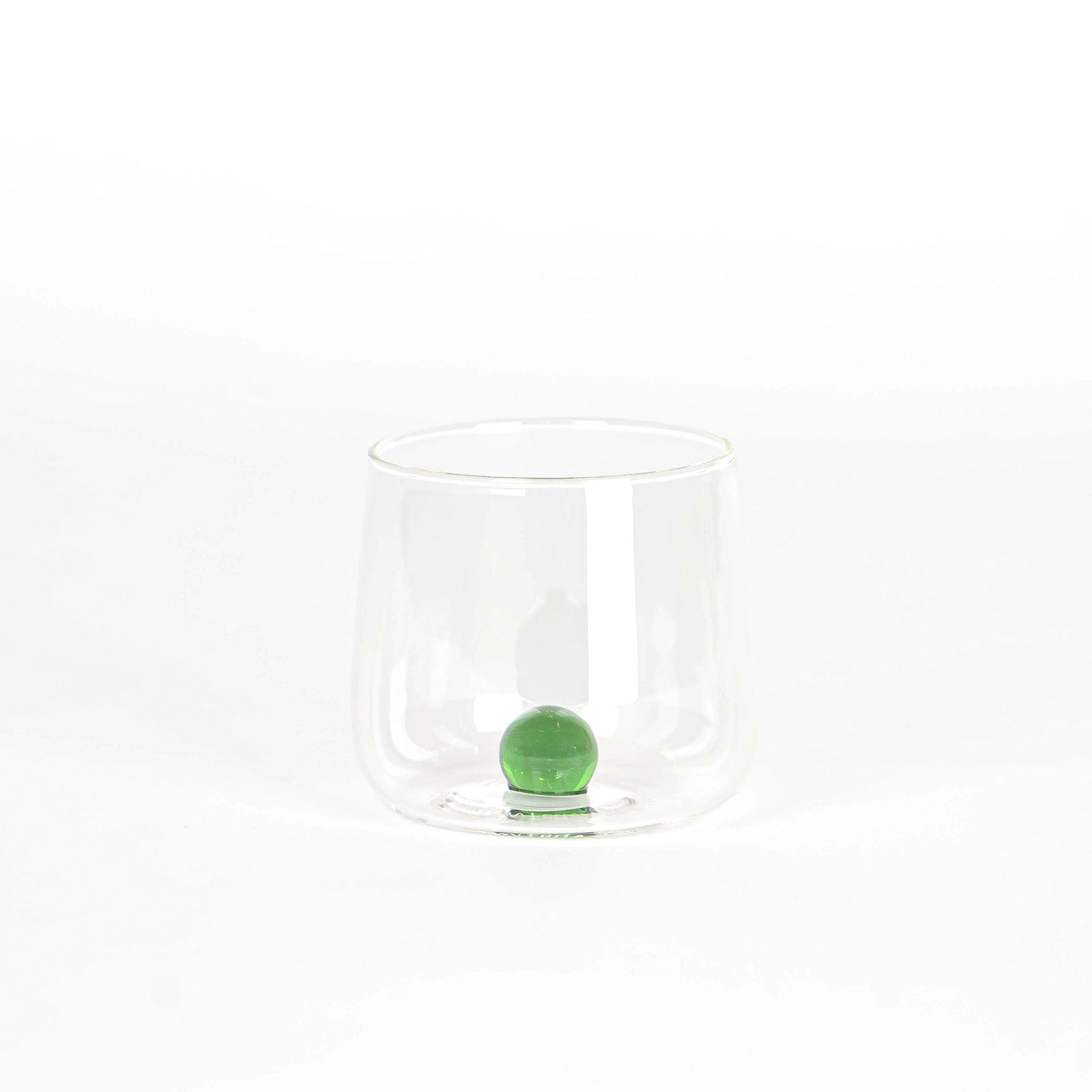 Bicchiere trasparente in vetro con base tonda e sfera verde all'interno, su sfondo bianco uniforme.