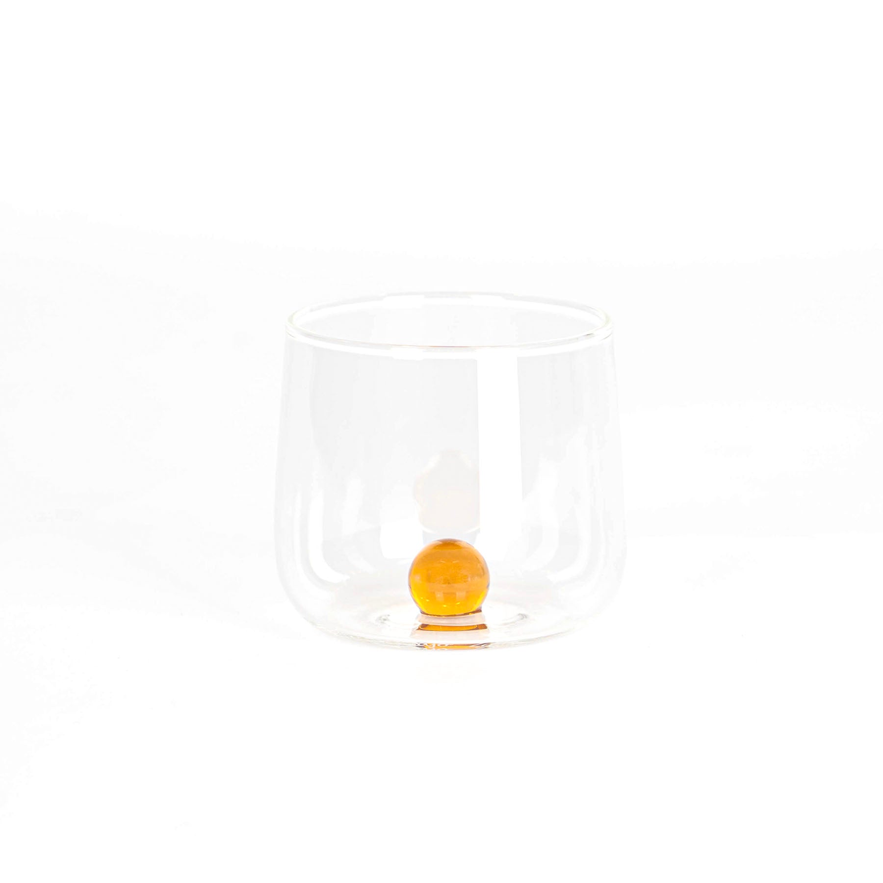 bicchiere trasparente in vetro con base arrotondata e sfera arancione all'interno su sfondo bianco chiaro