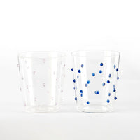 Due bicchieri trasparenti in vetro con puntini sporgenti, uno con punti rosa e l'altro con punti blu, su sfondo bianco.