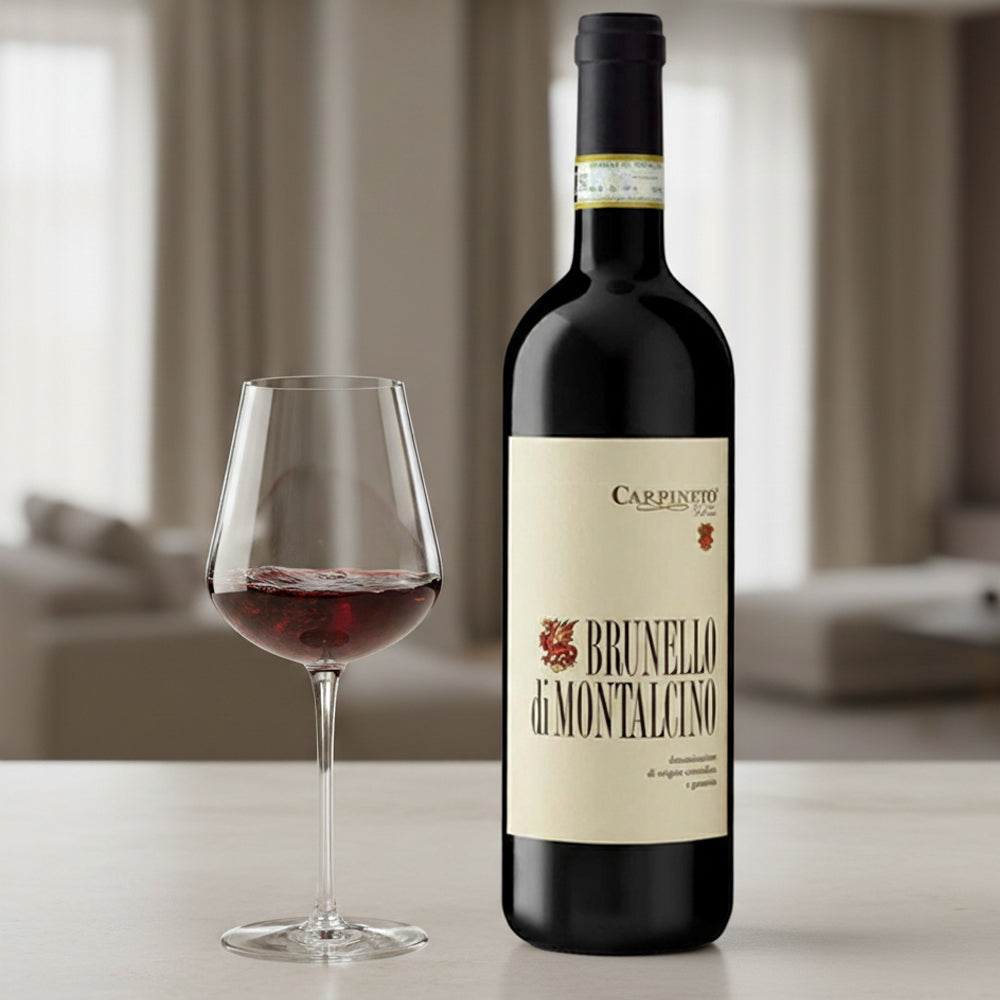 Bottiglia di vino rosso Brunello di Montalcino con etichetta beige, accanto a un bicchiere di vino, in un ambiente domestico elegante.