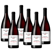Sei bottiglie di vino rosso, con etichetta bianca e dettagli neri, in un ambiente neutro.