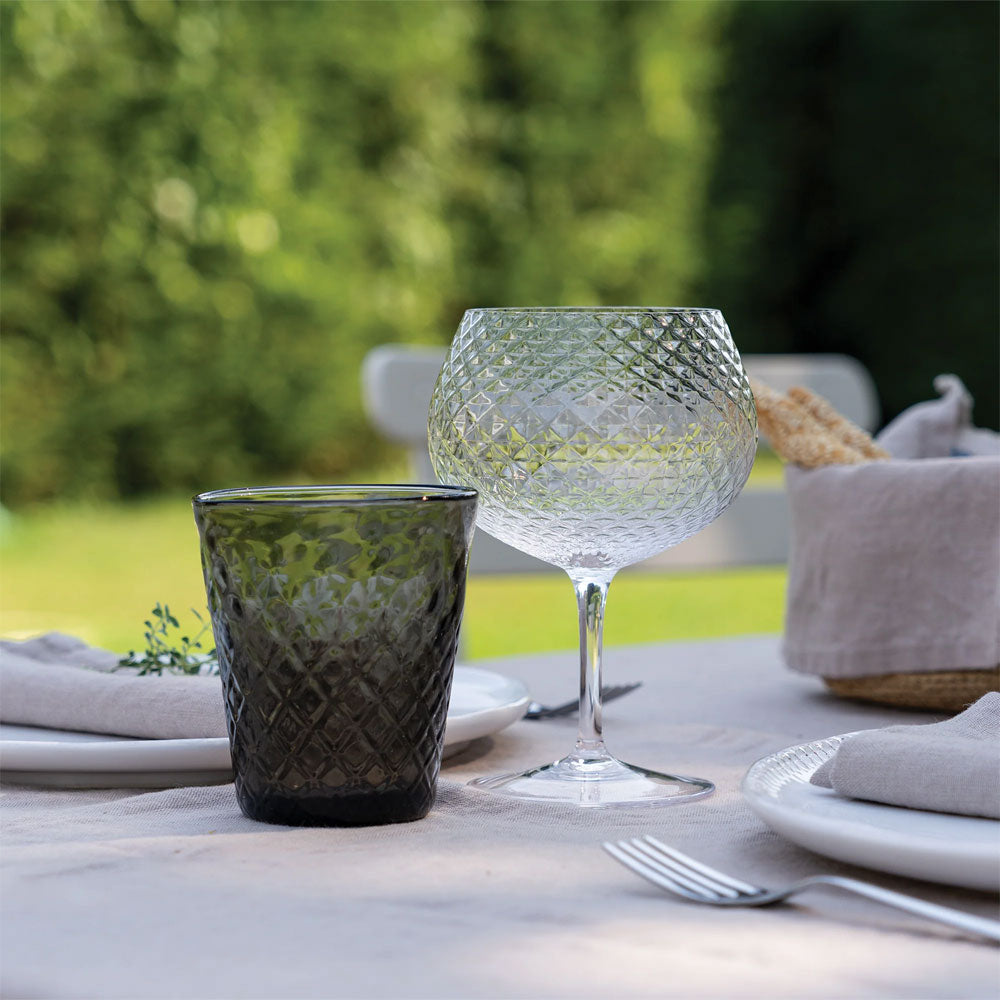 bicchiere da acqua in vetro verde scuro e calice da vino in vetro trasparente con superficie sfaccettata su tavola apparecchiata all'aperto