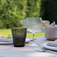 bicchiere da acqua in vetro verde scuro e calice da vino in vetro trasparente con superficie sfaccettata su tavola apparecchiata all'aperto