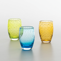 tre bicchieri di vetro colorato verde, azzurro e ambra con decorazione a rilievo a puntini su sfondo neutro chiaro