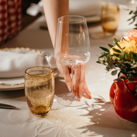 Bicchiere da vino trasparente in vetro sottile con mano che lo prende, bicchiere ambrato con bolle e vaso rosso con fiori gialli e