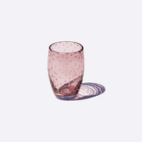 Bicchiere rosa trasparente in vetro con bolle interne, su sfondo bianco con ombra riflessa.