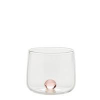 bicchiere trasparente in vetro con pallina rosa incastonata sul fondo, sfondo bianco neutro
