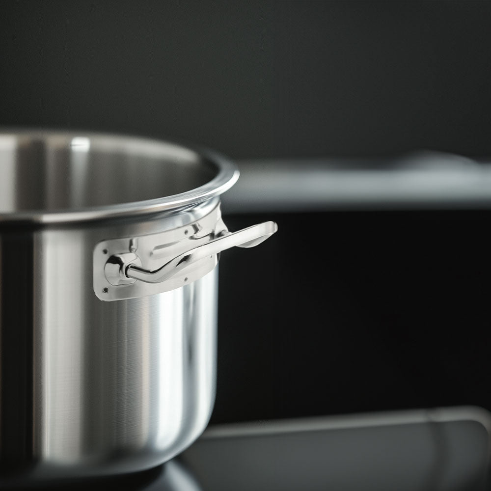 Pentola in acciaio inox lucido con manico corto, posizionata su piano cottura nero in ambiente cucina scura.