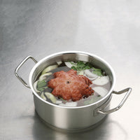 pentola in acciaio con gambo di polpo rosso, fette di cipolla, sedano e prezzemolo immersi in acqua, su piano metallico grigio riflettente