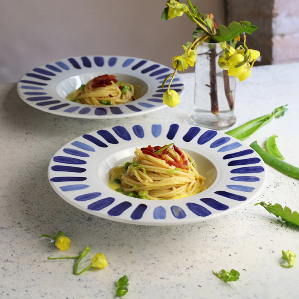 Due piatti bianchi in ceramica con bordo decorato a pennellate blu, contenenti spaghetti con piselli e pomodori secchi, su tavolo chiaro